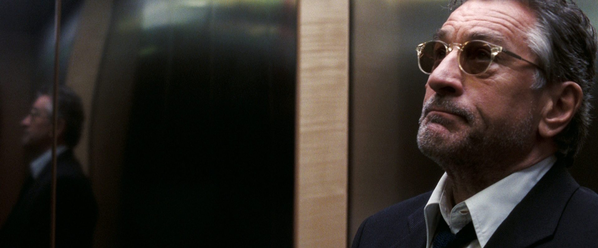 Nahaufnahme von Robert De Niro als Filmproduzent Ben mit Sonnenbrille im Fahrstuhl.