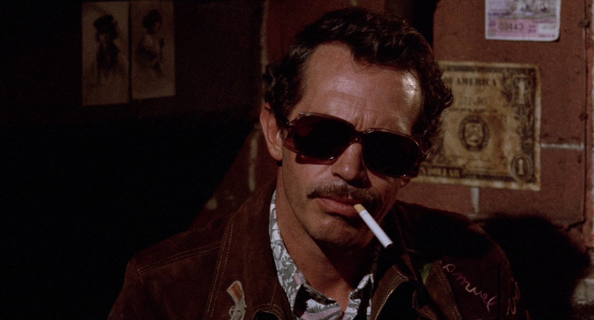 Nahaufnahme von Warren Oates als Bennie mit großer Sonnenbrille und Zigarette.